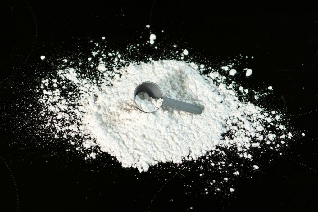 Black counter top with creatine powder in a messy pile and a small scoop lying on top.